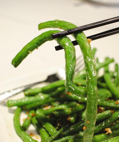 Stir fried green beans with garlic held by chopsticks